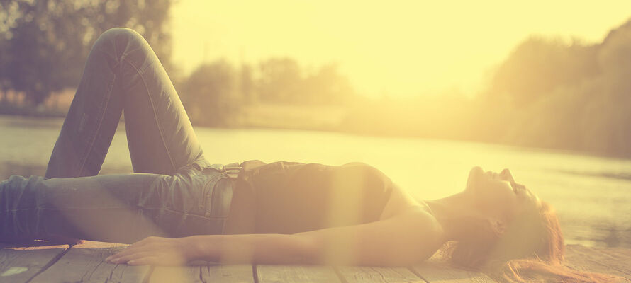 In der Sonne liegende Frau auf Holzsteg am See