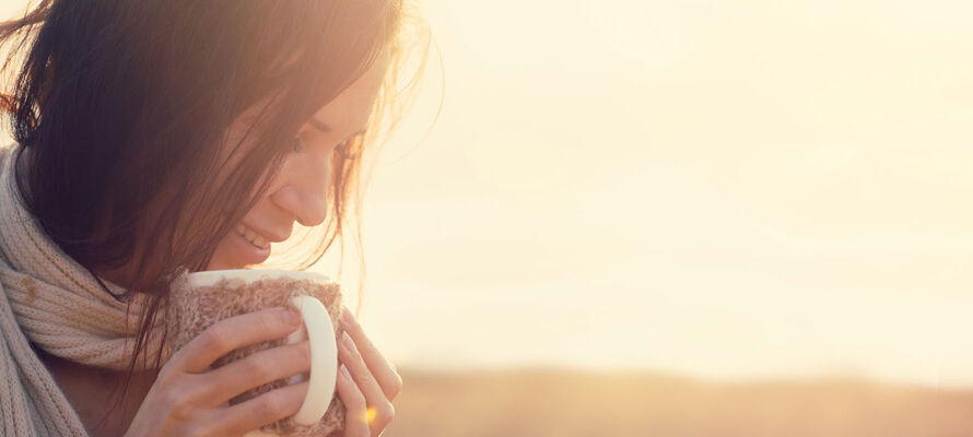 Frauengesicht mit wärmendem Getränk in den Händen im Garten